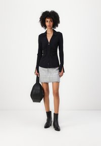 Maglietta nera a maniche lunghe con zip frontale e dettagli arricciati, abbinata a una mini gonna in tweed grigia con bordi frangiati e stivaletti neri alla caviglia.