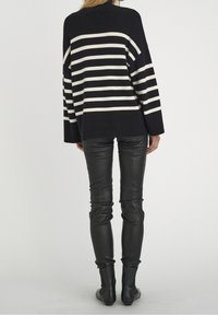 Suéter de gran tamaño a rayas blancas y negras con un cuello acanalado, acompañado de pantalones de cuero negro ajustados y botas de tobillo.
