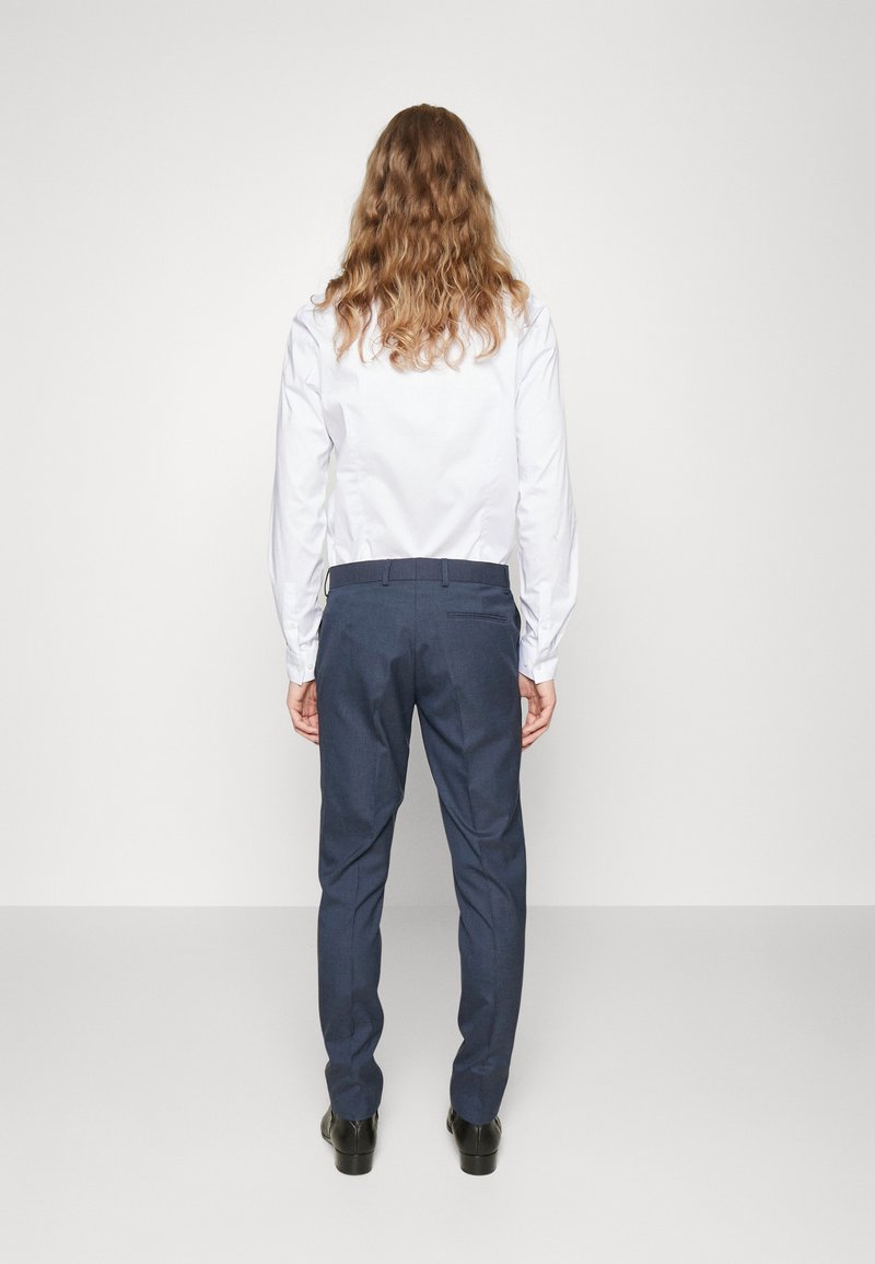 Camicia bianca a maniche lunghe abbinata a pantaloni su misura blu scuro, caratterizzati da linee pulite, texture liscia e dettagli di cucitura sottili.