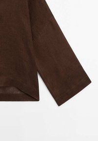 Chemise marron à manches longues avec un poignet droit et une fente triangulaire à l'ourlet sur fond blanc.