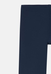Gros plan sur des leggings courts ajustés bleu marine montrant la ceinture et la partie supérieure de la cuisse sur un fond blanc.