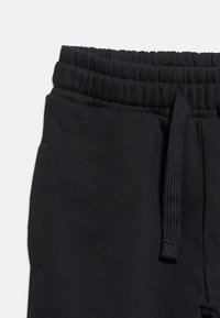 Μαύρο παντελόνι φόρμας με ελαστική μέση, μπροστινή τσέπη και μαύρο κορδόνι που φαίνεται στη δεξιά πλευρά.