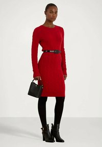 Κόκκινο φόρεμα με πλέξη κασμίρι και μακριά μανίκια, σε συνδυασμό με μαύρη ζώνη. Συνδυάζεται με μαύρες καλσόν και μποτάκια ως τον αστράγαλο. Περιλαμβάνεται και μικρή μαύρη τσάντα.