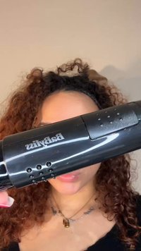 Sèche-cheveux noir avec une finition brillante, doté d'une prise texturée, de multiples trous pour le flux d'air, et d'un logo de marque bien visible sur le côté.