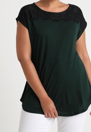 Top verde scuro con un accento di pizzo nero lungo la scollatura. Maniche corte e vestibilità rilassata con tessuto morbido.