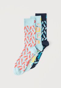 Τρία ζευγάρια πολύχρωμες κάλτσες με σχέδια ψαριών και κουτιών σαρδέλας, τοποθετημένες αλληλοκαλυπτόμενες σε ανοιχτό φόντο.