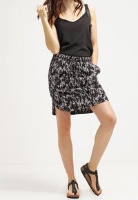Černý top na ramínka spárovaný s šedou a černou mini sukní se vzorem, která má elastický pas, šňůrku a postranní rozparky. Černé sandály.