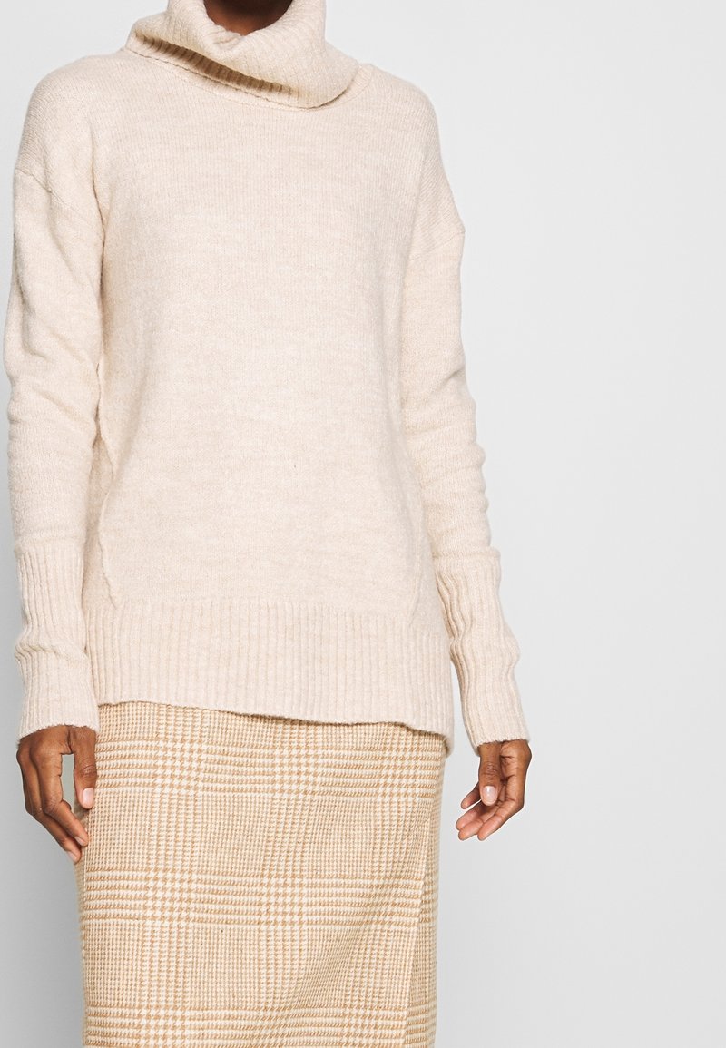 Hellbeige Rollkragensweater aus weichem Strickstoff, mit gerippten Bündchen und Saum. Kombiniert mit einem karierten hellbeigen Rock.