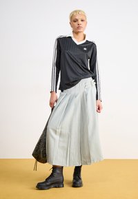 Μαύρο μπλουζάκι με μακριά μανίκια και λευκές ρίγες, με V λαιμόκοψη και γιακά. Γκρίζα πτυχωτή φούστα με αγκράφες και μαύρες δερμάτινες μπότες με κορδόνια.