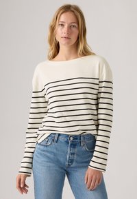 Gestreifter Strickpullover in Creme mit schwarzen horizontalen Streifen. Bietet eine entspannte Passform, einen runden Ausschnitt und lange Ärmel. Getragen mit blauen Jeans.