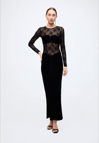 Black velvet dress with long lace sleeves and a fitted bodice. Features ruched detailing and a flowing skirt. Elegant design with contrasting textures.