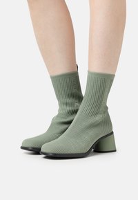 Botas de tobillo verdes de punto con una superficie texturada, un tacón cuadrado y un diseño de punta elegante. Presentan tela acanalada y un tacón en contraste.