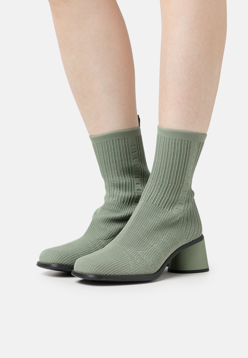 Botas de tobillo verdes de punto con una superficie texturada, un tacón cuadrado y un diseño de punta elegante. Presentan tela acanalada y un tacón en contraste.