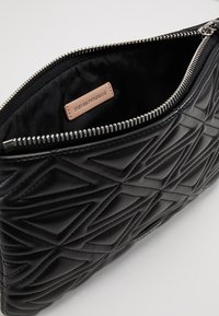 Černá prošívaná kabelka s stříbrným zipem, otevřená, aby ukázala černou látkovou podšívku a béžovou etiketu Emporio Armani.