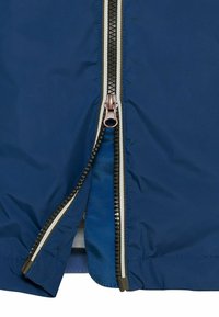 Veste bleue partiellement dézippée, montrant des dents de fermeture éclair noires et blanches avec un curseur en cuivre.