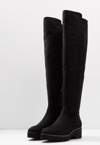 Botas negras hasta la rodilla hechas de suave ante, con una superficie texturizada, un tacón grueso y una cremallera lateral para ponerlas fácilmente.