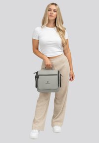 Borsa a tracolla grigia con zip nera, manico superiore ed emblema. Materiale sintetico liscio, forma quadrata e dettaglio con tasca frontale.