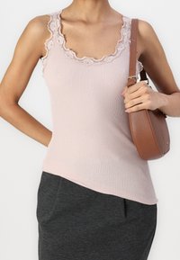 Světle růžový žebrovaný top s krajkovým lemem na výstřihu, doplněný tmavě šedou sukní a hnědou koženou kabelkou přes rameno.