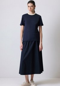 Mørkeblå bomulds t-shirt med en beige krave, parret med en matchende lang nederdel. Modellen har beige sneakers på. Enkel, afslappet pasform.