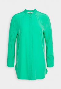 Blouse verte vif à manches longues avec col mandarin et boutons cachés à l'avant, présentée sur un fond blanc uni.
