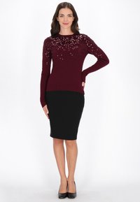 Pull en tricot bordeaux avec des détails en sequins aux épaules, associé à une jupe crayon noire et des escarpins noirs. Texture lisse, design ajusté.