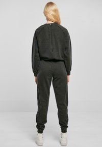 Mørkegrå zip-up jumpsuit med lange ermer, ribbede mansjetter og en tettsittende silhuett. Materialet ser mykt ut med en jevn tekstur.