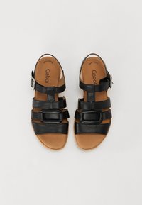 Sandales en cuir noir avec trois larges brides et une boucle décorative. Semelle intérieure marron avec le nom de la marque en relief. Texture lisse, design ouvert.