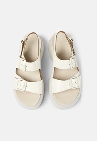 Bílé sandály vyrobené z hladké kůže s dvěma nastavitelnými přezkami, otevřeným špičkou a texturovanou světlebarevnou podrážkou.