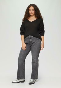 Zwarte gebreide trui met V-hals, gecombineerd met grijze flared jeans. Schoeisel bestaat uit zilveren, puntige enkellaarsjes met een lage hak.