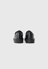 Black leather sneakers with a smooth texture, rounded back design, and rubber sole. Lacing system and subtle curved accents at the heel.