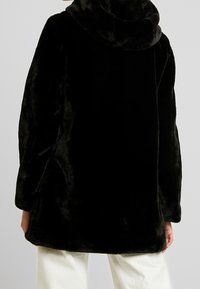 Abrigo de piel sintética negra con un cuello alto, que presenta un corte holgado y mangas largas; textura suave con un acabado liso.