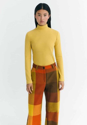 Ribbed yellow turtleneck sweater paired with wide-leg checkered pants featuring shades of orange, brown, and yellow. No visible hardware or patterns.