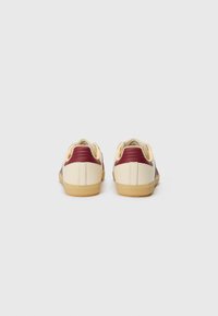 Cremefarvede og maroon læder sneakers med en tekstureret hæl, gummi sål og minimalistisk design. Har polstret ryg og buet form.