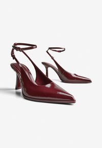 Burgundske lakirane slingback čevlje z ostrimi noski, trakci okoli gležnja in srednje visokimi špicastimi petami. Gladka tekstura in eleganten dizajn.
