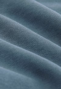 Strukturalna tkanina w miękkim niebieskim kolorze, ukazująca delikatne prążkowanie i gładką powierzchnię. Materiał wydaje się lekki z subtelnymi fałdami i cieniami.