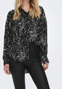 Zwarte en witte gestreepte blouse met een kraag, lange mouwen en een losse fit, gecombineerd met zwarte faux leren broek. Soepele textuur.