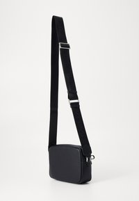 Borsa a tracolla nera con texture liscia, forma rettangolare, tracolla regolabile, hardware in argento e chiusura con zip.