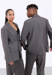 Completo grigio a righe con un design su misura, caratterizzato da una giacca a un petto e pantaloni dritti. Texture liscia e vestibilità strutturata.
