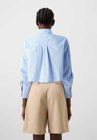 Blue striped cropped shirt with long sleeves and button cuffs, paired with beige tailored shorts. Smooth fabric with subtle texture.
