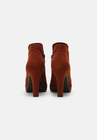 Braune Wildleder-Ankle Boots mit hohen Absätzen, seitlichem Reißverschluss und schickem Design, glatter Textur und abgerundeter Zehenpartie.
