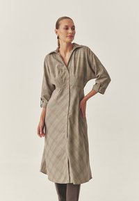 Vestito abbottonato con motivo a quadri, caratterizzato da maniche lunghe, collo con risvolto e vita aderente. Realizzato in tessuto leggero con una texture liscia.