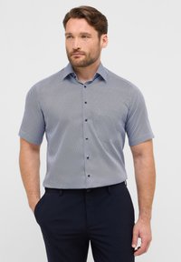 Camicia a maniche corte con bottoni in fantasia geometrica blu e bianca, realizzata in tessuto leggero con colletto a punta e bottoni blu.