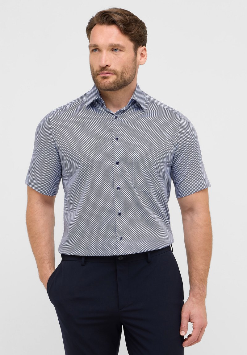 Camicia a maniche corte con bottoni in fantasia geometrica blu e bianca, realizzata in tessuto leggero con colletto a punta e bottoni blu.