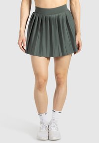 Falda plegada verde hecha de tela suave con cintura alta. La longitud es por encima de la rodilla, combinada con calcetines y zapatos deportivos blancos.