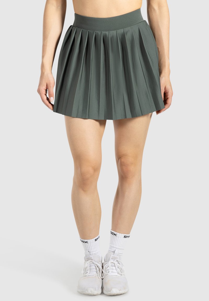 Falda plegada verde hecha de tela suave con cintura alta. La longitud es por encima de la rodilla, combinada con calcetines y zapatos deportivos blancos.