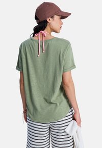 Grön t-shirt med korta ärmar och uppvikta ärmar, med ett rosa band i nacke. Kombination med mönstrade svart-vita byxor.