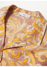 Blouse à manches courtes à motif floral en crème, pr ésentant des volutes jaunes vives et roses pâles, une texture lisse et un col classique. Étiquette MNG visible.