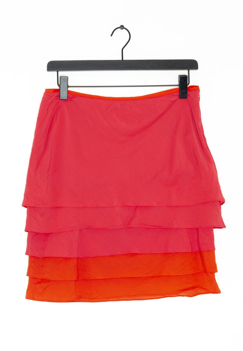 Jupe superposée rouge et orange suspendue à un cintre noir sur fond blanc.