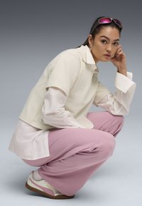 Off-white kortärmad texturerad topp över en vit skjorta, ihop med rosa vida byxor och krämfärgade sneakers med bruna sålar.