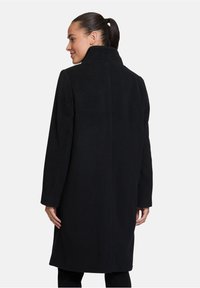 Cappotto di lana nero con colletto alto, maniche lunghe e silhouette dritta. Texture morbida e design minimalista senza hardware visibile.